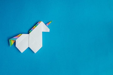 Handmade white trendy geometrical polygonal paper origami unicorn on blue background. Empty space. Horizontal poster, postcard, banner template.