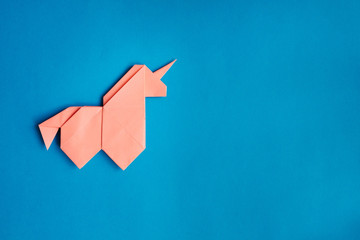 Handmade pink trendy geometrical polygonal paper origami unicorn on blue background. Empty space. Horizontal poster, postcard, banner template. © mykolastock