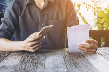 Hand of man asia Check bill with mobile phone . Pay for food after eating out .