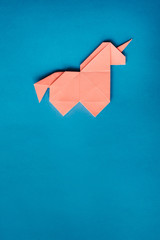 Handmade pink trendy geometrical polygonal paper origami unicorn on blue background. Empty space. Vertical poster, postcard, banner template. © mykolastock