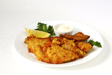 Golden batter deep fried fish fillets, served on white plate with sauce and lemon