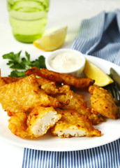 Golden batter deep fried fish fillets, served on white plate with sauce and lemon