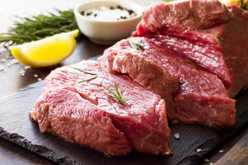 Fresh meat. Cheese steak beef on a slate cutting board, lemon, spices and fresh rosemary on a stone table.