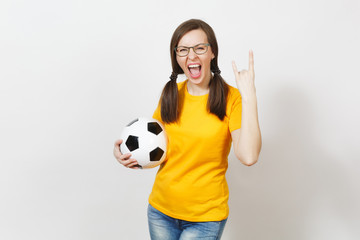 Smiling sport European woman, two fun pony tails, football fan or player in glasses, yellow uniform, depict heavy metal rock sign, horns gesture, hold classic soccer ball isolated on white background.