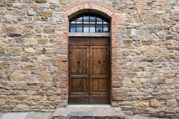 Fototapeta na wymiar Wooden door with class panel transom in ancient stone wall