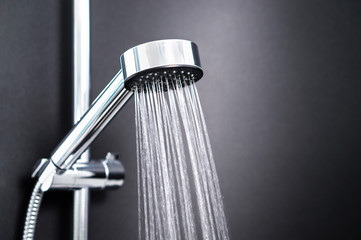 Water running from shower head in bathroom with dark black background. Simple stylish and modern...