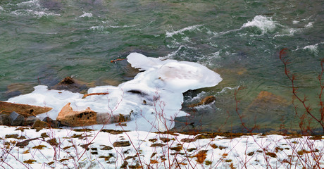 verschneites Flussufer mit schmelzendem Eis