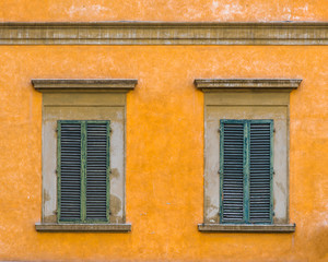 Fototapeta na wymiar Closed windows in yellow wall with green shutters