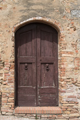 Fototapeta na wymiar Old wooden door in sunlight set in brick wall