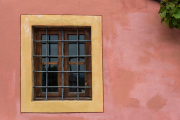 Fototapeta na wymiar Gated closed window on pink textured wall with yellow frame