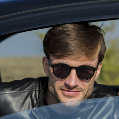 cute young man in sunglasses smiling and looking out of an open car window.