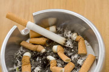Ashtray full of extinguished cigarette butts with one lit