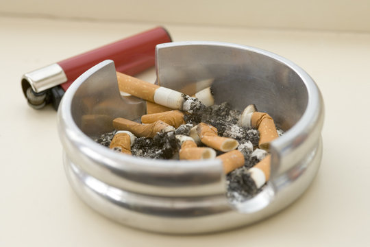 Ashtray full of extinguished cigarette butts with one lit