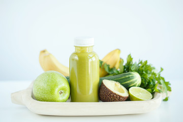  wooden tray with ingredients for a green smoothie in a bottle, a banana, an apple, lime, parsley, avocado, cucumber