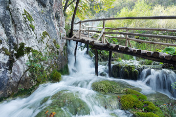 A boardwalk built above a waterfall with a cliff on the left side. The water is rushing right under the wooden boardwalk. 
