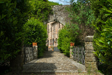 Ancient iron gate in a stone wall over a shrub covered bridge in Rural  Italy