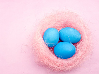 Color easter eggs in pink nest on pastel background.