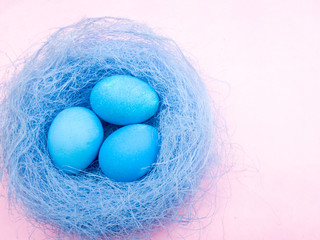 Blue easter eggs in nest on pastel pink background.