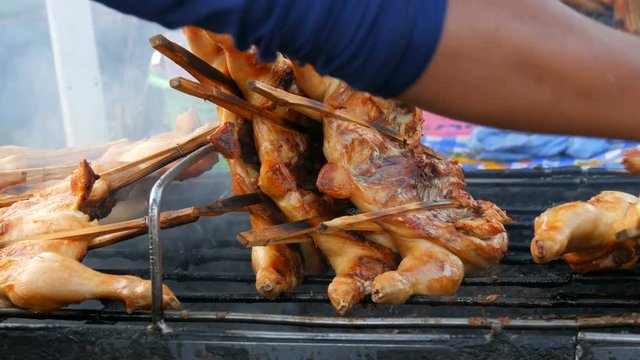 Whole chicken carcass grill strung on wooden stick grilling on the grill. Street Food Thailand. Men's hands turn over the grilled chicken