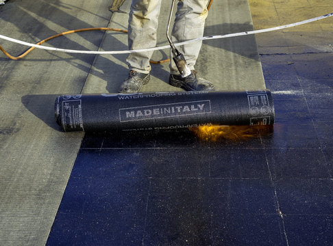 Worker preparing part of bitumen roofing felt roll for melting by gas heater torch flame