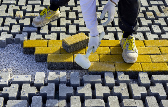 Construction worker laying interlocking paving concrete onto sheet nonwoven bedding sand and fitting them into place.