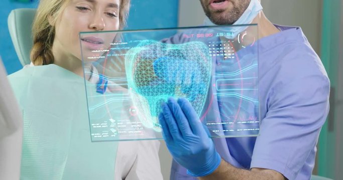 A futuristic dentist shows the futuristic holographic plate of the patient's dentition, and she smiles happily. Concept of: dentists, healthcare, medical examination, technology, future.