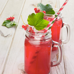 Homemade red currant lemonade in a mason jar with decor of berry on ligth wooden table.