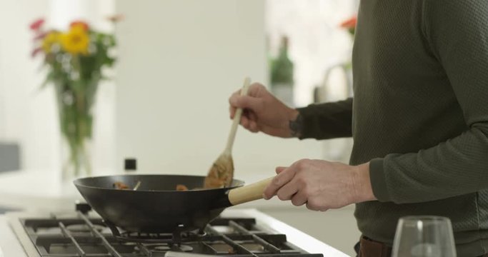 4K Cheerful single man cooking at home with glass of wine, following a recipe on computer tablet