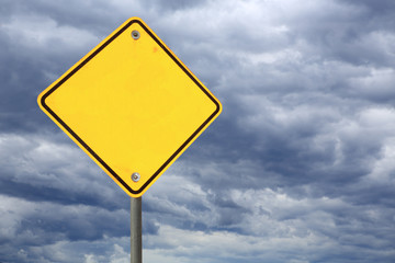 empty yellow road warning sign against a dark stormy sky 