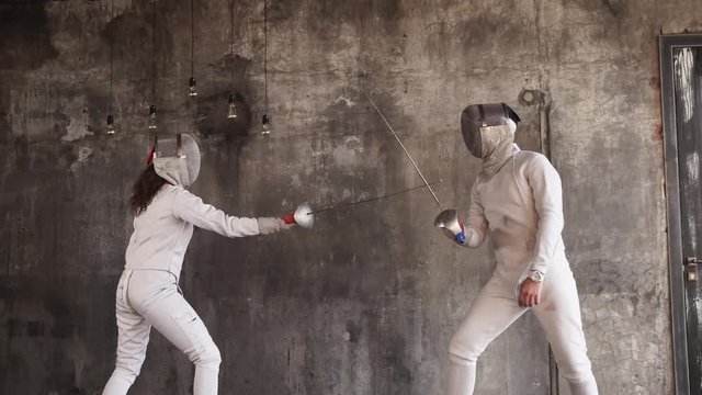 a man and a woman are engaged in fencing in a protective suit, a lady and her rival actively prick each other with a sword in the fitness club