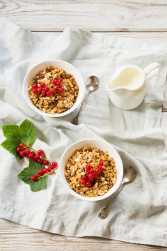 Summer healthy breakfast for two person of granola, muesli on light wooden board. Milk jug and red currant as decor. Top view.