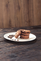 chocolate chip cookies on a white plate with coffee beans on dark wooden table