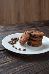 chocolate chip cookies on a white plate with coffee beans on dark wooden table