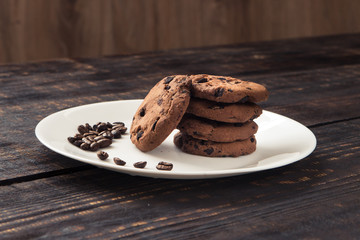 chocolate chip cookies on a white plate with coffee beans on dark wooden table