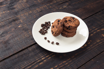 chocolate chip cookies on a white plate with coffee beans on dark wooden table