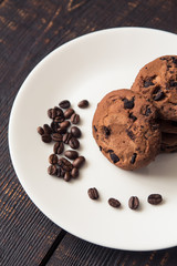 chocolate chip cookies on a white plate with coffee beans on dark wooden table