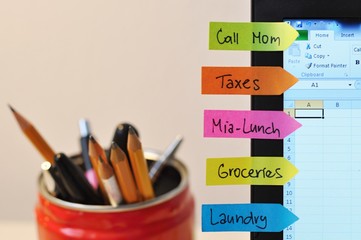 to do list written on funny colorful stickers on a laptop display, organization of the daily tasks, with pens and pencils in the background