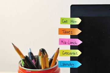 to do list written on funny colorful stickers on a laptop display, organization of the daily tasks, with pens and pencils in the background