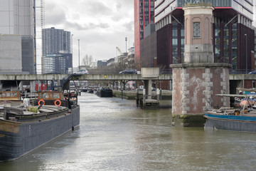 Details of old harbor of Rotterdam in cloudy day in November at low tide illustrating modern urban landscape with water, ships and tall buildings, Rotterdam, Netherlands.
