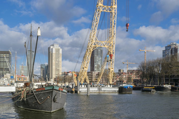 Skyline of Rotterdam in sunny day in November as seen from old harbor with ships and vintage industrial machines illustrating modern urban landscape with water, ships and buildings, Netherlands.
