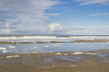Low tide at Scheveningen beach near the Hague featuring cargo ships on horizon under dark sky clouds. North sea background in January. The Netherlands.