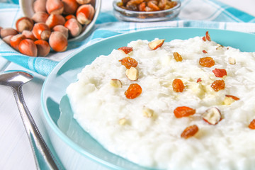 Rice milk porridge with nuts and raisins in a blue dish on a white wooden table.