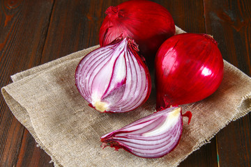 Fresh red onions and chopped slices on a wooden table.