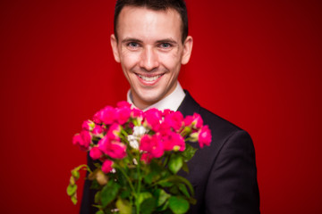 Stylish man in suit holding a bouquet of flowers with red background