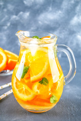 Fototapeta na wymiar Orange detox water in a pitcher on a gray concrete background. Healthy food, drinks.