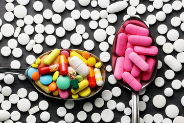 Colorful pills in spoons and pink pills