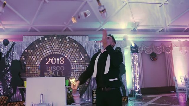 A professional bartender juggles with three bottles of fire at a disco party. The bartender is impressive, it's wonderful show on the holiday