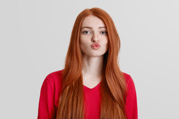 Adorable red haired female with freckled skin, rounds lips, going to kiss someone, has long redish...