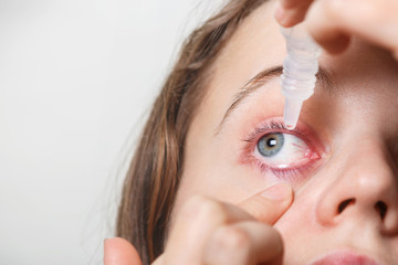 Female puts eye drop in her inflamated red eye, suffers from conjuctivitis, isolated on white. Woman applies eye drops. Eye treatment and health concept