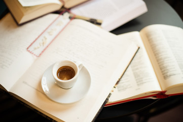 front view Cup of espresso among a lot of opened books sun light in background front view Cup of espresso among a lot of opened books sun light in background